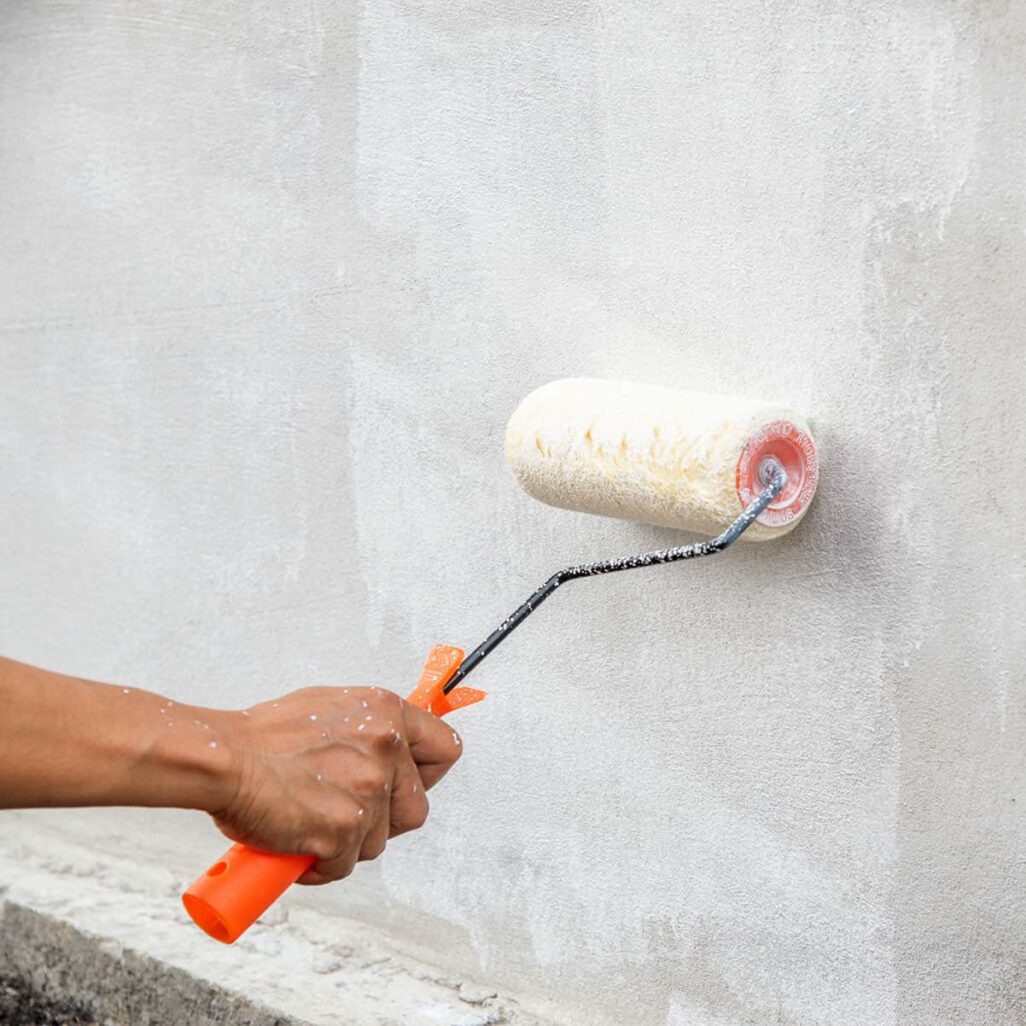 Personne appliquant de la peinture blanche sur un mur elle-même, méthode DIY non recommandée par Batitprotect