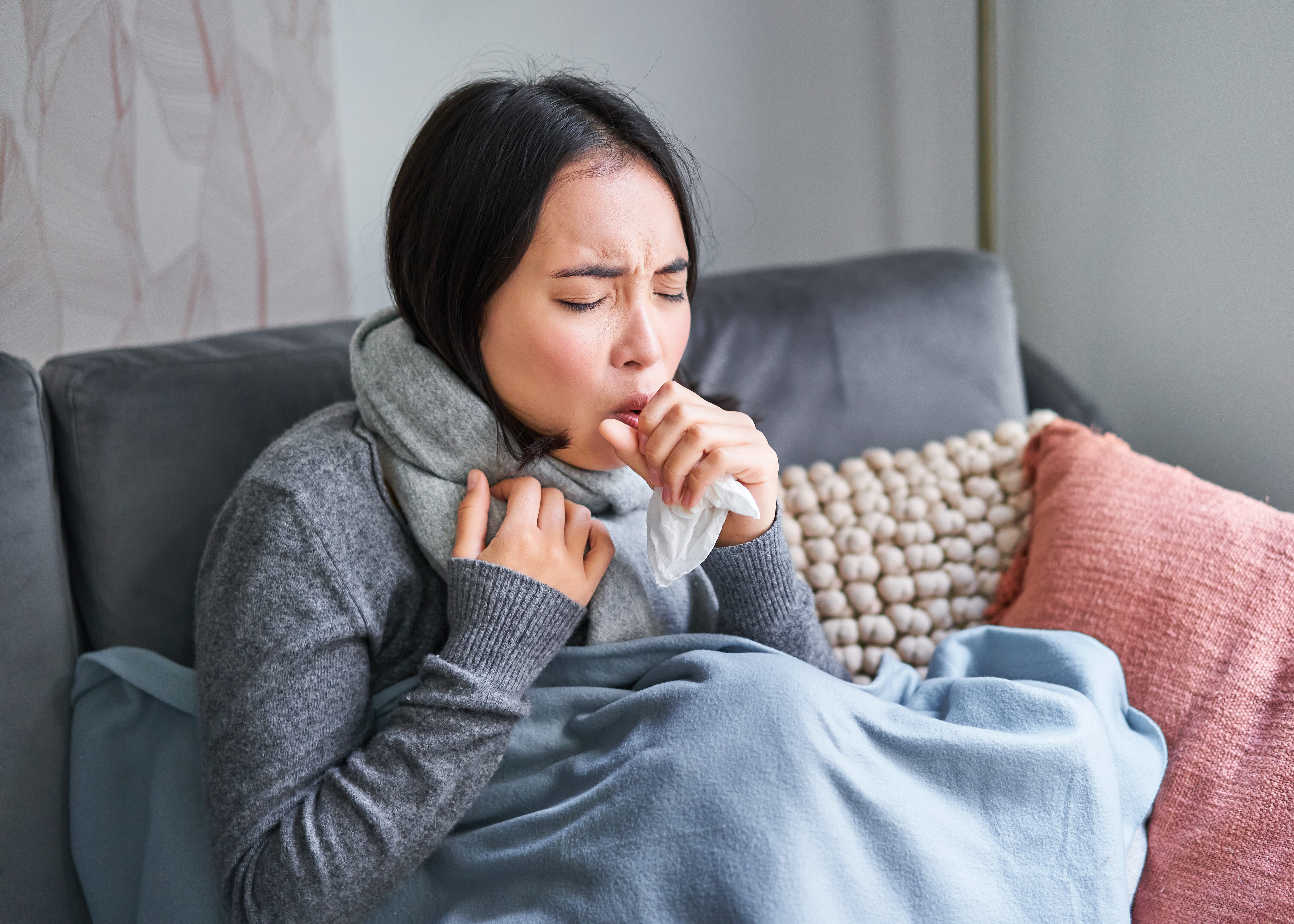 Femme malade assise sous une couverture dans un appartement froid, symptômes de grippe